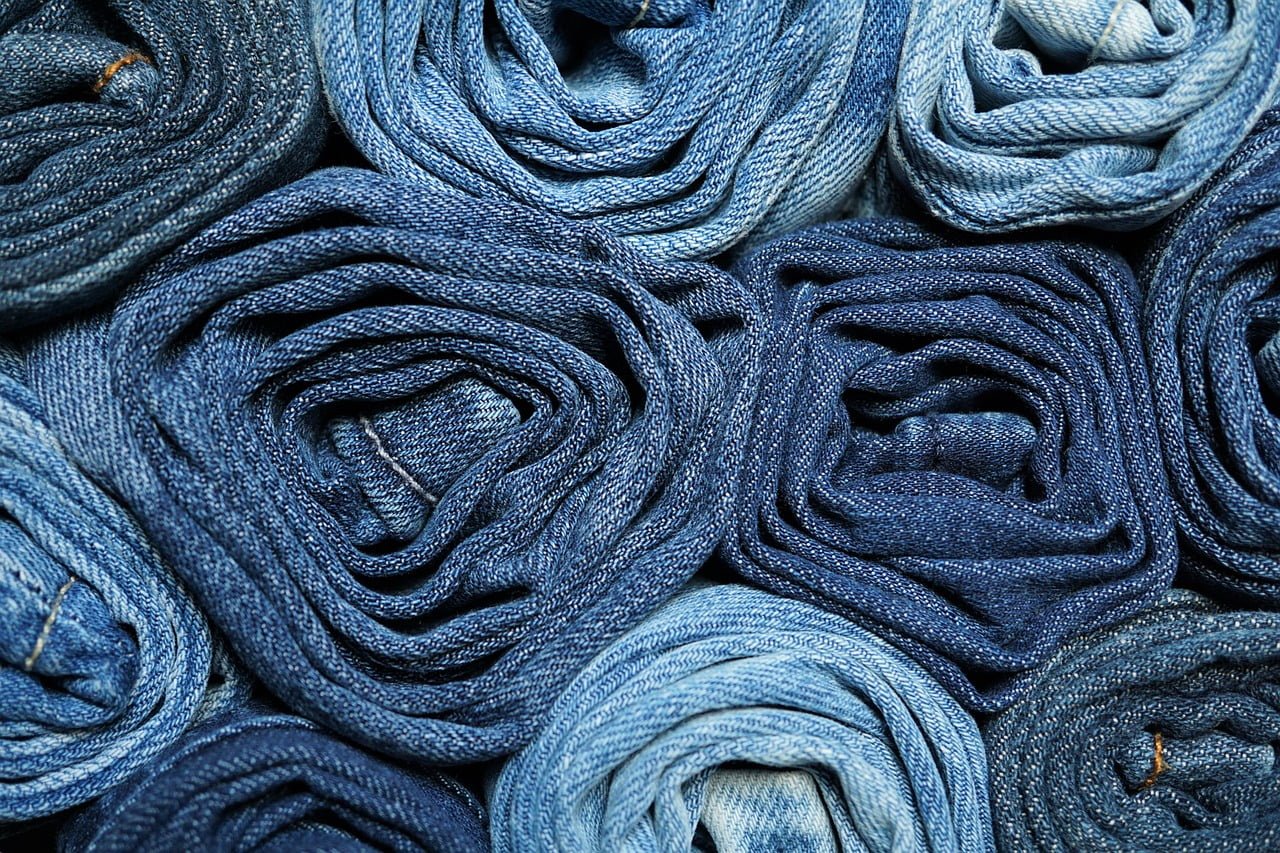 Rolled-up denim jeans arranged closely together, forming a textured pattern. The jeans vary in shades of blue, from light to dark, showcasing the different hues of denim fabric. A versatile choice for fashion tips on wide leg jeans that can flatter any silhouette, especially over 40.